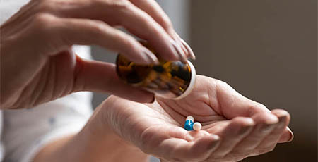 A lady shakes capsules from a medicine bottle into her palm.
