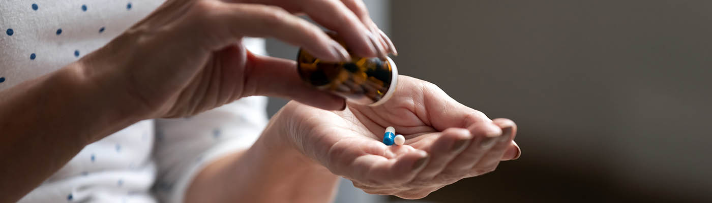 A woman shaking tablets from a bottle into her hand.